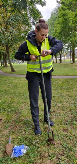 A woman in a yellow hi viz jacket taking a soil core in an urban park